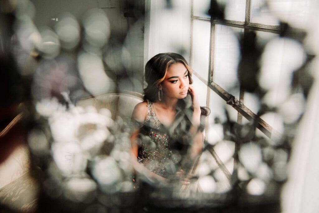 The female subject can be seen through the silhouette of a crown as she sits on a gold antique sette looking out of windows